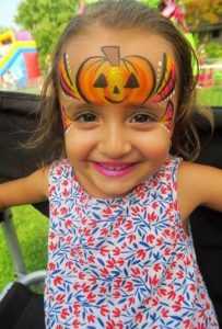 child with face painting of pumpkin at fall event
