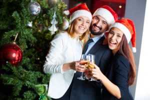 company christmas party guests with santa hats by holiday tree