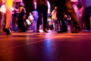 A low shot of the dance floor with a crowd dancing at an event under the colorful lights